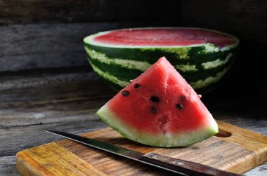 Karpuz, dilimlenmiş, bıçak, mutfak tahtası eski bir rustik masada.