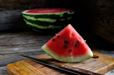 Karpuz, dilimlenmiş, bıçak, mutfak tahtası eski bir rustik masada.