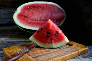 Karpuz, dilimlenmiş, bıçak, mutfak tahtası eski bir rustik masada.