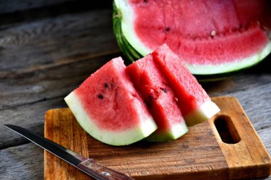 Karpuz, dilimlenmiş, bıçak, mutfak tahtası eski bir rustik masada.