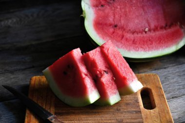 Karpuz, dilimlenmiş, bıçak, mutfak tahtası eski bir rustik masada.