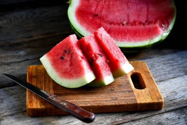 Karpuz, dilimlenmiş, bıçak, mutfak tahtası eski bir rustik masada.