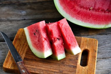 Karpuz, dilimlenmiş, bıçak, mutfak tahtası eski bir rustik masada.