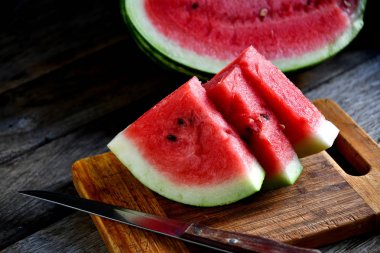 Karpuz, dilimlenmiş, bıçak, mutfak tahtası eski bir rustik masada.