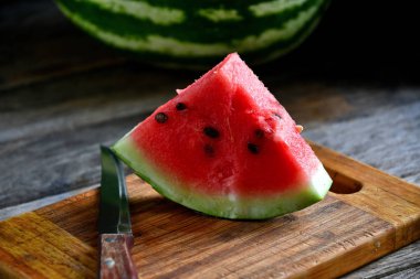 Karpuz, dilimlenmiş, bıçak, mutfak tahtası eski bir rustik masada.