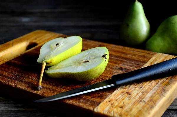 Sliced pear on a kitchen board and knife on a rustic table.