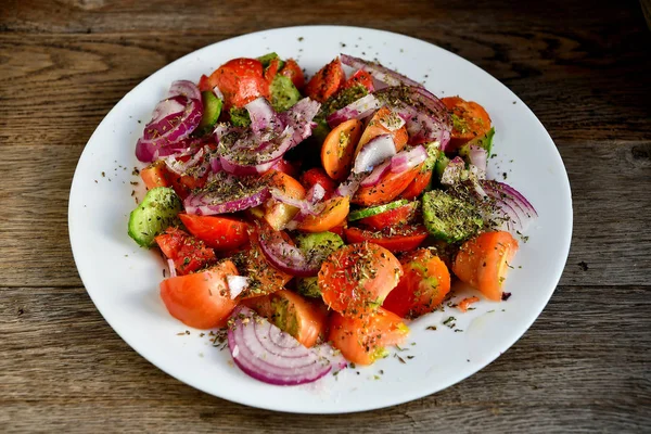 Ahşap bir masa üzerinde beyaz bir tabakta domates, salatalık, baharat ve otlar Yaz salatası.