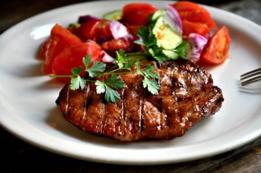 Domuz biftek, salata domates, beyaz bir tabak tabaktabak tabaktabak tabaktabak salatalık yeşillik çeşniler.