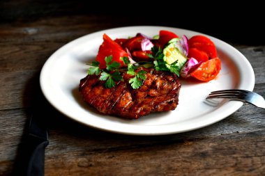 Domuz biftek, salata domates, beyaz bir tabak tabaktabak tabaktabak tabaktabak salatalık yeşillik çeşniler.