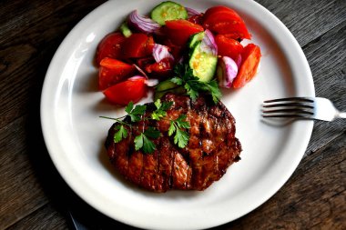 Domuz biftek, salata domates, beyaz bir tabak tabaktabak tabaktabak tabaktabak salatalık yeşillik çeşniler.