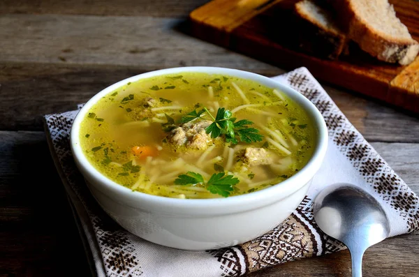 Homemade soup with meatballs and noodles, folk napkin on a wooden table.