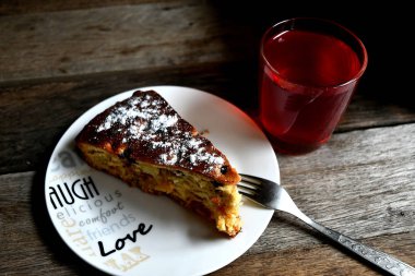 Charlotte beyaz bir tabak, çatal ve ahşap bir masa üzerinde elma kompostosu.