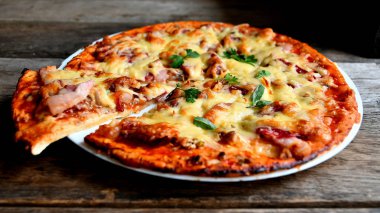 Ahşap bir masa üzerinde beyaz bir seramik tabakta peynir, domates, pastırma ve otlar ile ev yapımı pizza.