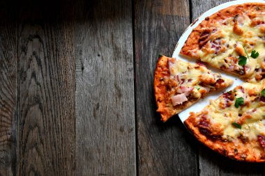 Ahşap bir masa üzerinde beyaz bir seramik tabakta peynir, domates, pastırma ve otlar ile ev yapımı pizza.