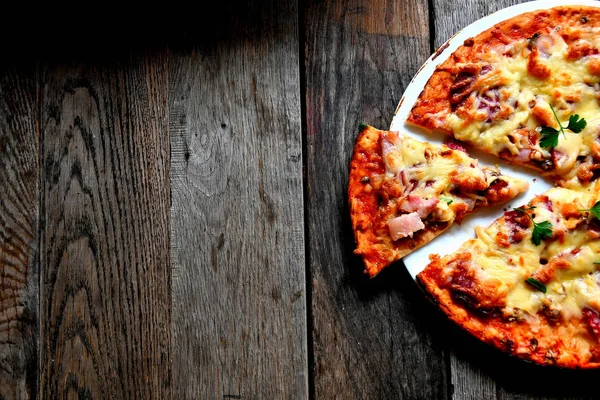 Ahşap bir masa üzerinde beyaz bir seramik tabakta peynir, domates, pastırma ve otlar ile ev yapımı pizza.