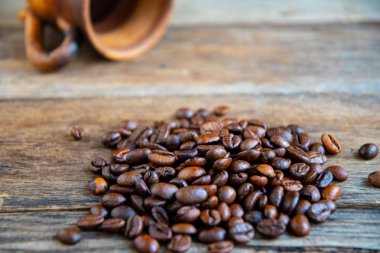 Kavrulmuş kahve çekirdekleri seramik bir fincandan eski tahtalara saçılmış..