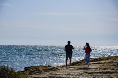 Bir kız ve bir adam deniz kenarında bir kayanın üzerinde yürüyorlar..
