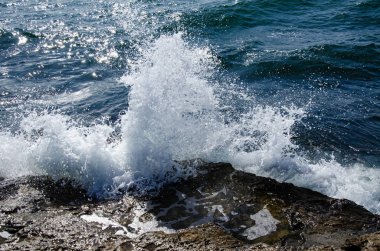 Güneşli bir günde bir kayanın üzerinde bir dalga kırılır..