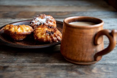 Seramik bardakta sütlü kahve, ahşap masada seramik kasede ev yapımı kek..