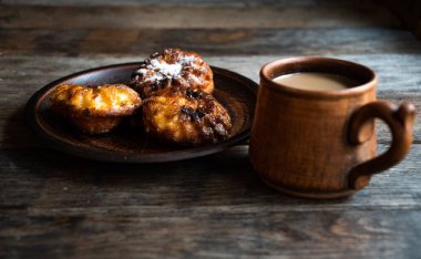 Seramik bardakta sütlü kahve, ahşap masada seramik kasede ev yapımı kek..