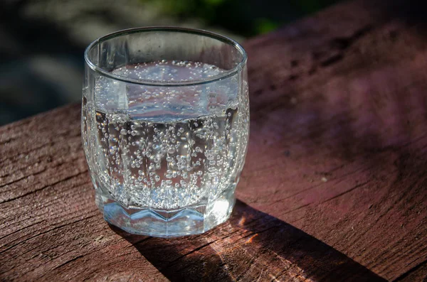 A glass with mineral, carbonated water on a wooden board in the garden.