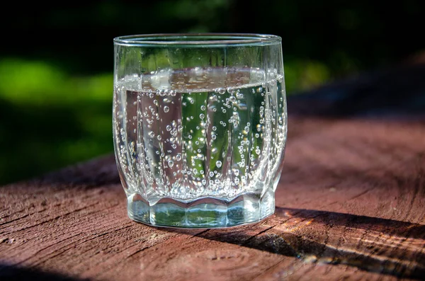 A glass with mineral, carbonated water on a wooden board in the garden.