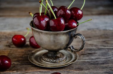 Tahta bir arka planda gümüş bir fincanda kırmızı kiraz meyveleri..