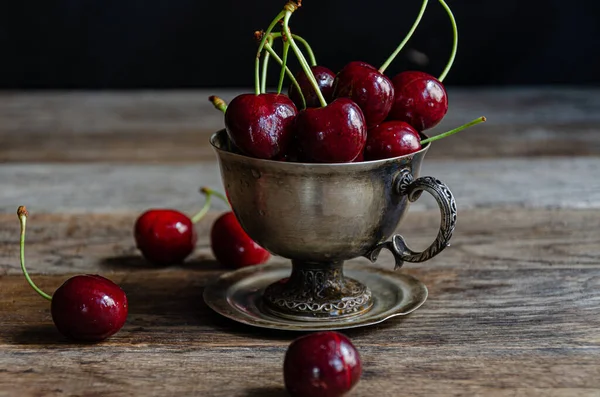 Tahta bir arka planda gümüş bir fincanda kırmızı kiraz meyveleri..