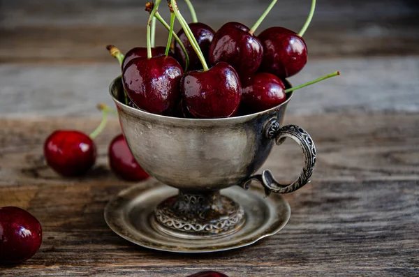 Tahta bir arka planda gümüş bir fincanda kırmızı kiraz meyveleri..