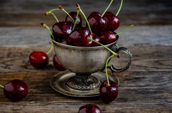 Tahta bir arka planda gümüş bir fincanda kırmızı kiraz meyveleri..