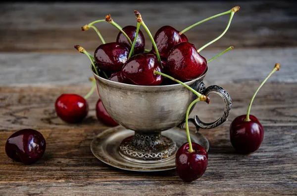 Tahta bir arka planda gümüş bir fincanda kırmızı kiraz meyveleri..