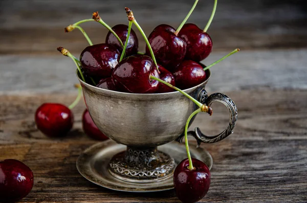 Tahta bir arka planda gümüş bir fincanda kırmızı kiraz meyveleri..