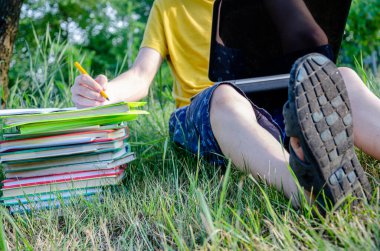 Adam bir öğrenci, bir öğrenci nişanlanmış, internetteki ağacın altındaki bahçede dizüstü bilgisayarla ödev yapıyor..