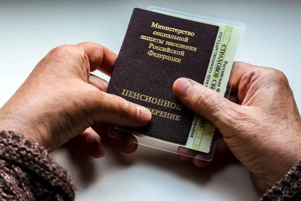 Woman\'s hand holding russian pension certificate. Russian translation - Ministry of Social Protection of Population of Russian Federation. Pension Certificate.