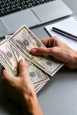 Yüz elli dolarlık banknotları tutan eller, arka planda dizüstü bilgisayarlar..