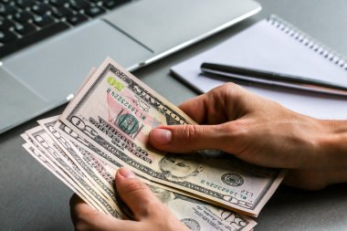 Yüz elli dolarlık banknotları tutan eller, arka planda dizüstü bilgisayarlar..