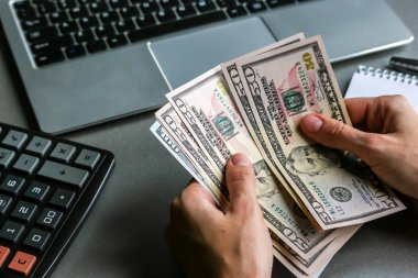 Yüz elli dolarlık banknotları tutan eller, arka planda dizüstü bilgisayarlar..