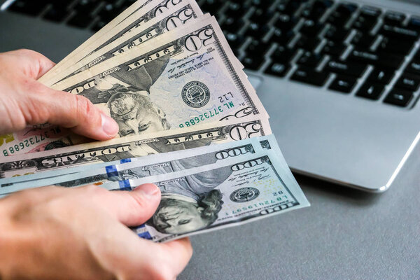 Рука держит банкноты за 150 долларов, ноутбук клавиатуру в фоновом режиме
.