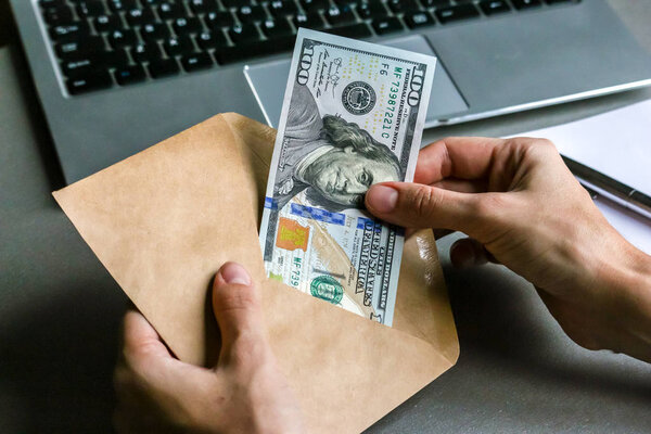 Руки держать конверт с банкнотой сто долларов, ноутбук клавиатуры в фоновом режиме
.