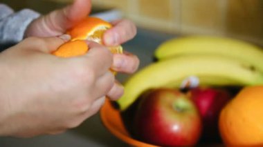 Kadınların elleri arka planda bir sepet meyve ile mandalina kabuğunu soyarlar.