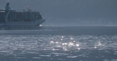büyük yolcu yolcu gemisi yavaş yavaş su yüzeyinde güneş parlaması ile Kotor körfezi üzerinde süzülür