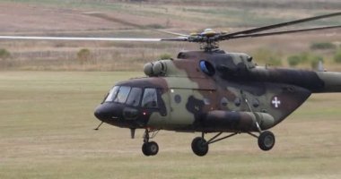 a military transport helicopter landing slowly on the grass