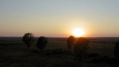 Bulutsuz ve rüzgarlı bir günde arka planda günbatımı olan büyük tarlalar üzerinde İHA ile uçmak