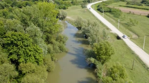 雲のない晴れた日の道路の横に川の真ん中にカヤックの漕ぎと小さな泥だらけの川の上にドローンで飛行 — ストック動画