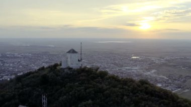 Güzel bir günbatımının, tepenin üstünde bir kulenin ve tepenin altında bir şehrin insansız hava aracı görüntüsü.