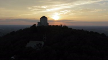 Gün batımında dağın tepesindeki taş bir ortaçağ kulesi. Güneşin kule arkasında çekildiği drone uçuşu.