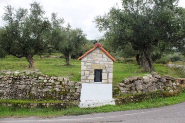 Yunanistan 'ın güneybatısındaki Messinia bölgesinde arka planda zeytin koruluğuyla mum yakmak için kullanılan küçük ölçekli kilise benzeri bir ikonostaz..