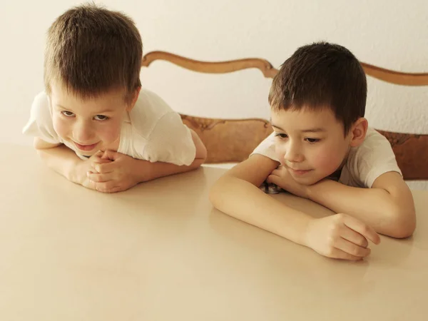 Dwóch chłopców w biały siedzi przy stole na jasne tło zbliżenie. Koncepcja rodziny — Zdjęcie stockowe