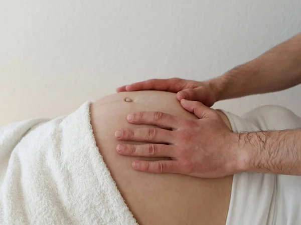 一个孕妇的大肚子, 她躺在她的背上穿着白色的衣服。肚子上是雄性手。特写. — 图库照片