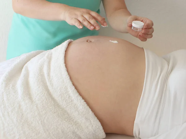 Tenendo le mani di una giovane donna ha aperto una fiaschetta di crema bianca e l'uso della pancia nuda di una donna incinta. Prenditi cura di tuo figlio. Primo piano . — Foto Stock